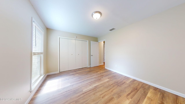 unfurnished bedroom featuring multiple windows, a closet, and light wood-type flooring