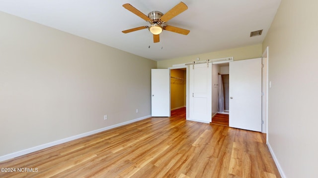 unfurnished bedroom featuring ceiling fan, light hardwood / wood-style flooring, a closet, a barn door, and a walk in closet