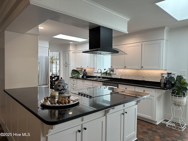 kitchen featuring a skylight, island range hood, decorative backsplash, white cabinets, and freestanding refrigerator