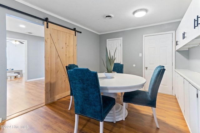 dining space featuring ceiling fan, light hardwood / wood-style floors, a barn door, and ornamental molding