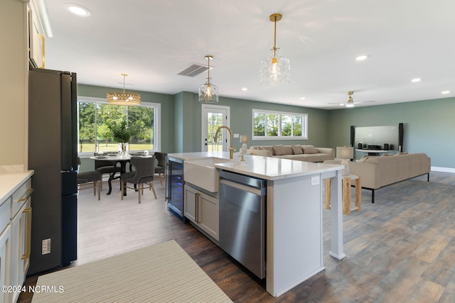 kitchen with pendant lighting, dishwasher, a center island with sink, sink, and fridge