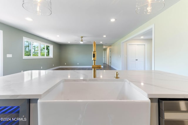 kitchen with light stone countertops, ceiling fan with notable chandelier, hanging light fixtures, and sink