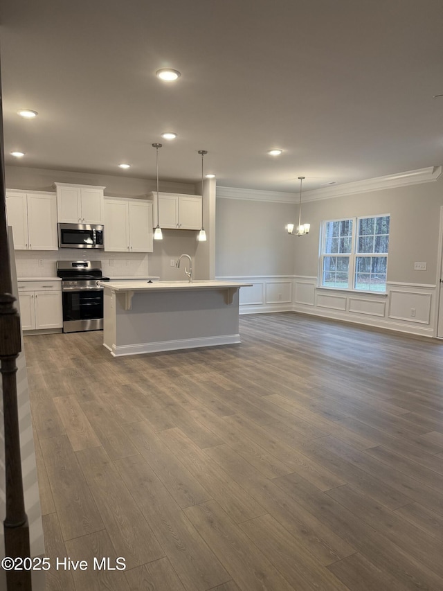 kitchen with pendant lighting, appliances with stainless steel finishes, white cabinetry, a center island with sink, and crown molding