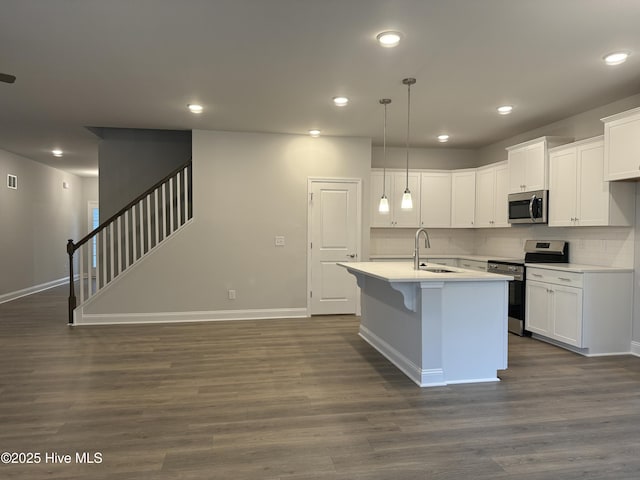 kitchen featuring white cabinets, decorative light fixtures, stainless steel appliances, an island with sink, and sink