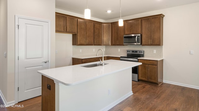 kitchen featuring dark hardwood / wood-style floors, an island with sink, stainless steel appliances, sink, and pendant lighting