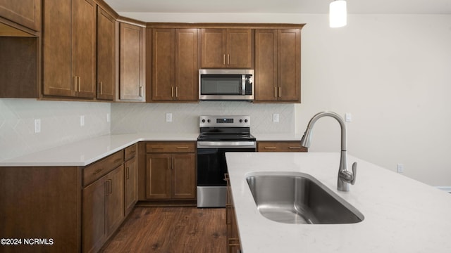 kitchen with sink, stainless steel appliances, pendant lighting, dark wood-type flooring, and decorative backsplash