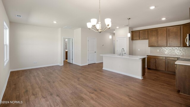 kitchen featuring dark hardwood / wood-style floors, an inviting chandelier, decorative light fixtures, and a center island with sink