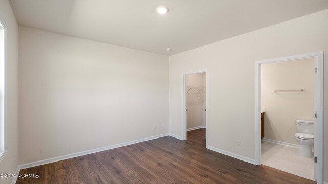 unfurnished bedroom featuring a closet, connected bathroom, dark hardwood / wood-style floors, and a walk in closet