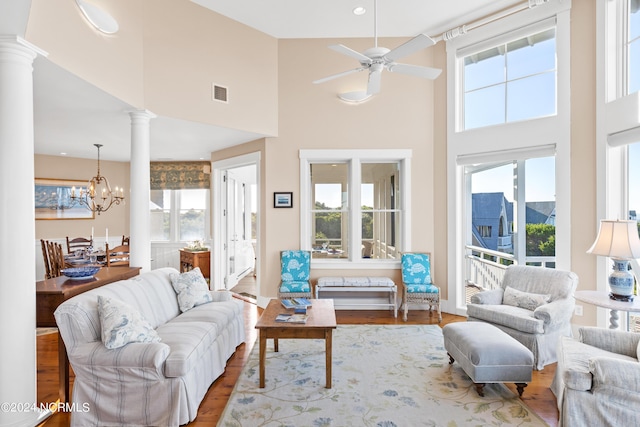 living room with ornate columns, a towering ceiling, wood-type flooring, and ceiling fan with notable chandelier