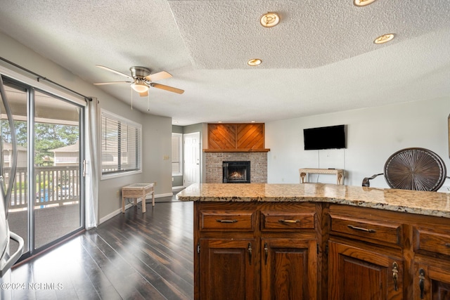 kitchen featuring a textured ceiling, dark hardwood / wood-style floors, light stone counters, and ceiling fan