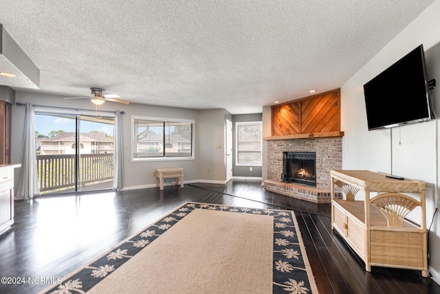 living room featuring a textured ceiling, dark hardwood / wood-style floors, a brick fireplace, and ceiling fan