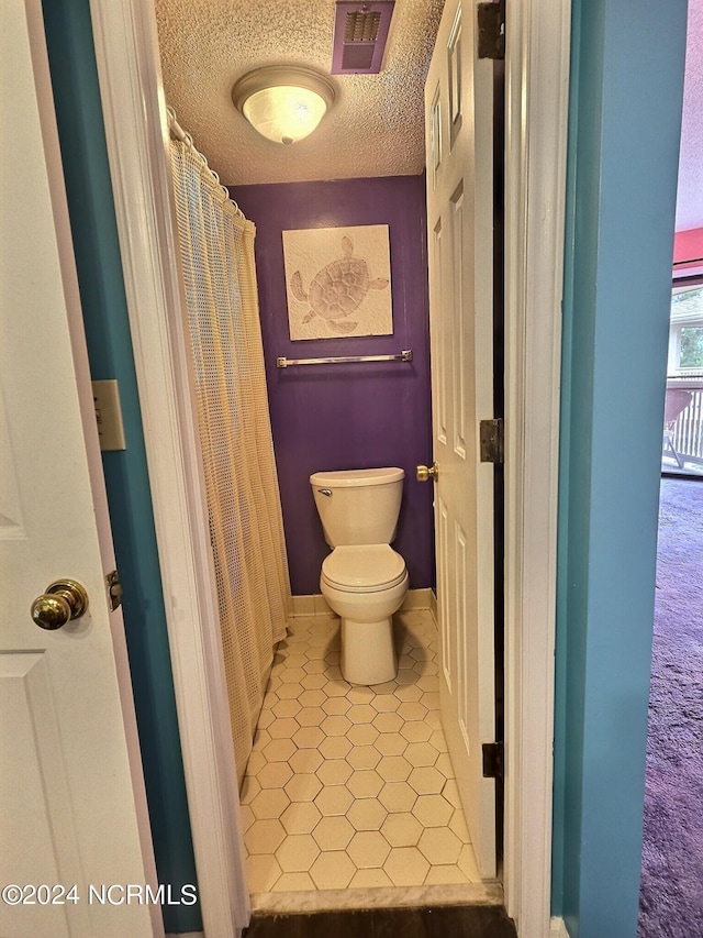 bathroom with tile patterned flooring, a textured ceiling, and toilet