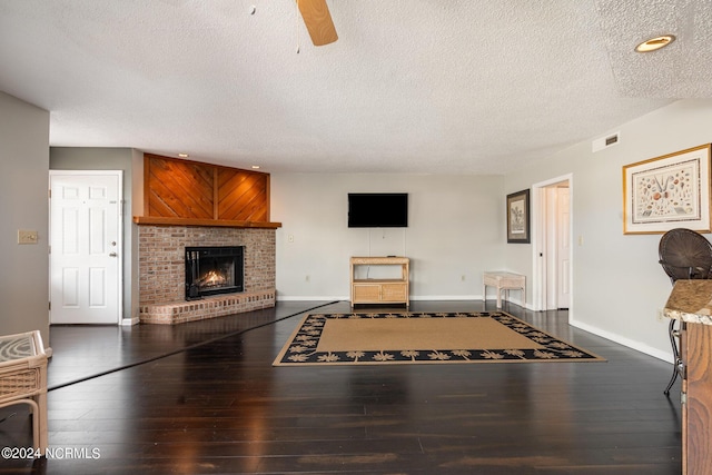 living room with ceiling fan, dark hardwood / wood-style floors, a textured ceiling, and a brick fireplace