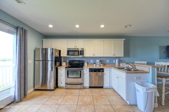 kitchen featuring decorative backsplash, appliances with stainless steel finishes, a peninsula, a sink, and light tile patterned flooring