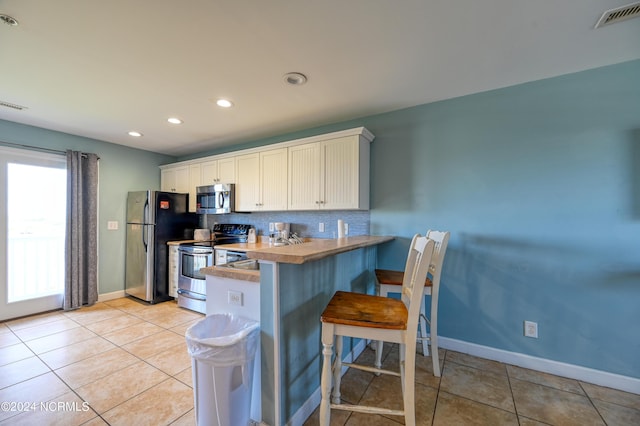 kitchen with visible vents, decorative backsplash, a breakfast bar area, stainless steel appliances, and light tile patterned flooring