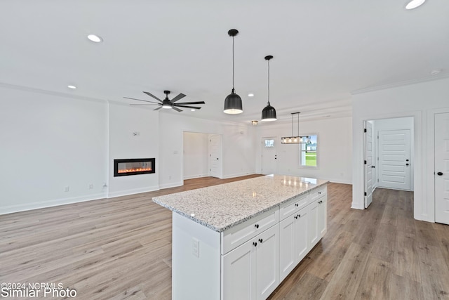 kitchen featuring white cabinets, hanging light fixtures, light hardwood / wood-style flooring, light stone countertops, and ceiling fan