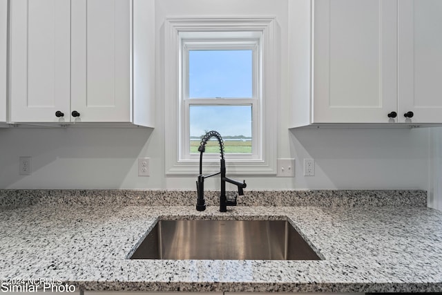 kitchen featuring white cabinets, light stone counters, and sink