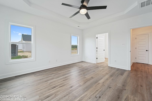 unfurnished room with a raised ceiling, light hardwood / wood-style flooring, ceiling fan, and a wealth of natural light