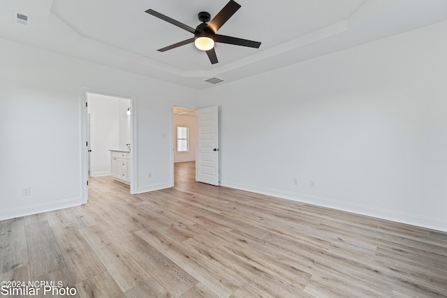 unfurnished bedroom with light hardwood / wood-style flooring, a tray ceiling, ceiling fan, and ensuite bathroom