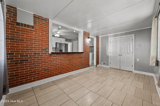 interior space with stainless steel fridge, ceiling fan, and brick wall