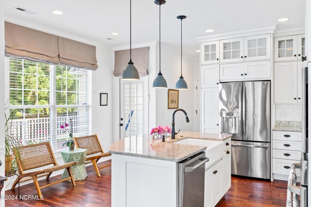 kitchen featuring light stone counters, pendant lighting, stainless steel appliances, a kitchen island with sink, and white cabinets