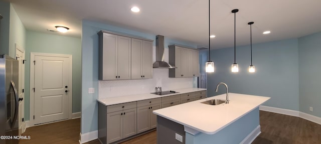 kitchen featuring sink, stainless steel refrigerator, a center island with sink, decorative light fixtures, and wall chimney exhaust hood