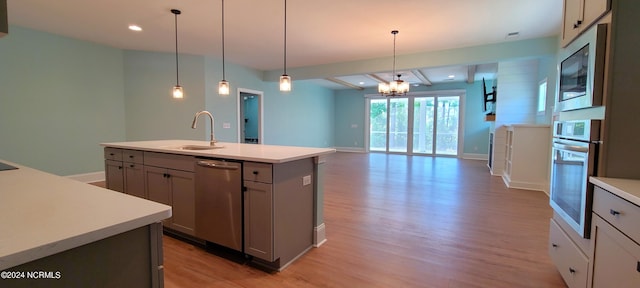 kitchen with gray cabinets, an island with sink, sink, hanging light fixtures, and stainless steel appliances