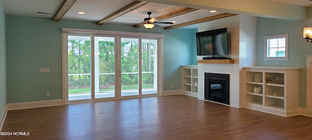 unfurnished living room featuring beam ceiling, dark hardwood / wood-style floors, a large fireplace, and a healthy amount of sunlight