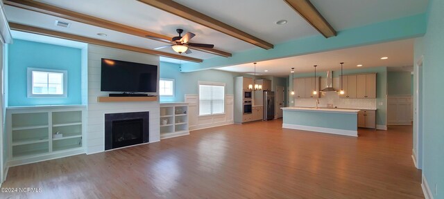 unfurnished living room featuring sink, ceiling fan with notable chandelier, a large fireplace, light hardwood / wood-style floors, and beam ceiling