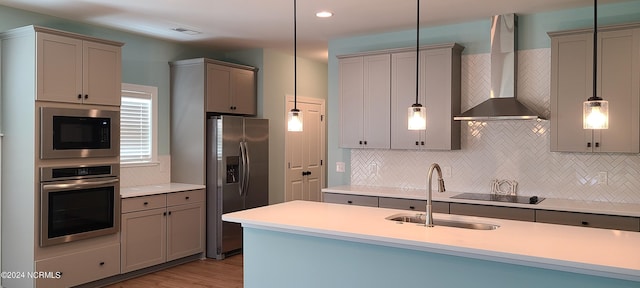 kitchen with wall chimney range hood, decorative light fixtures, stainless steel appliances, and sink