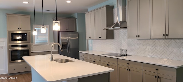 kitchen featuring wall chimney exhaust hood, sink, hanging light fixtures, an island with sink, and black appliances