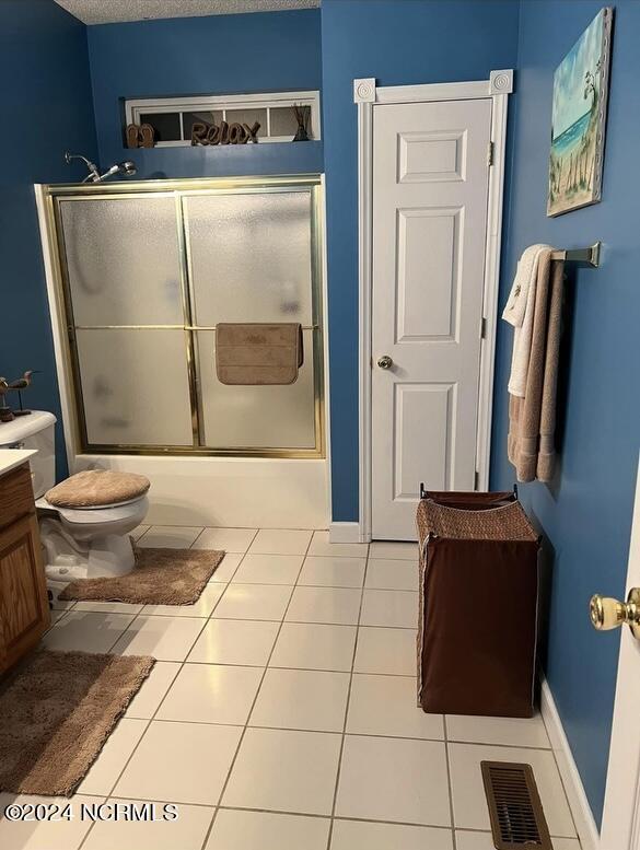 full bathroom featuring shower / bath combination with glass door, vanity, toilet, tile patterned floors, and a textured ceiling