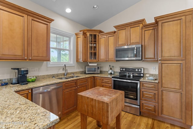 kitchen featuring lofted ceiling, sink, stainless steel appliances, light stone countertops, and light wood-type flooring