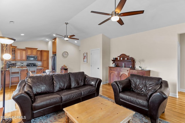 living room with vaulted ceiling, ceiling fan, and light wood-type flooring