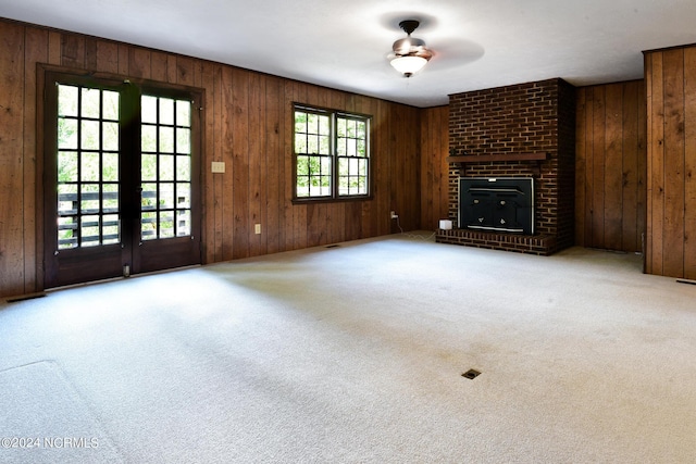 unfurnished living room with french doors, a brick fireplace, carpet flooring, and wooden walls