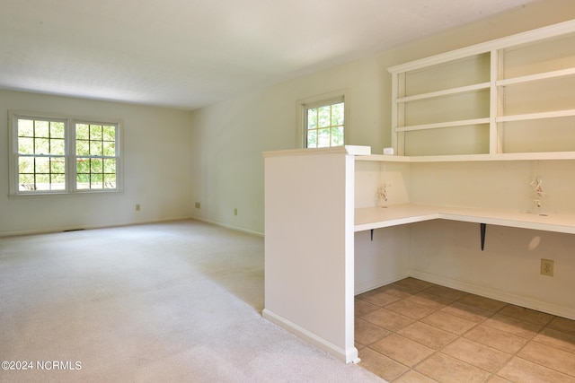 unfurnished room with light colored carpet, built in study area, and baseboards