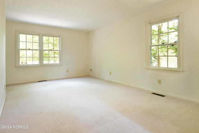 carpeted empty room featuring plenty of natural light, visible vents, and baseboards