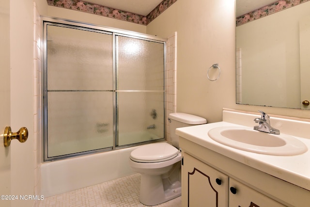 bathroom featuring toilet, combined bath / shower with glass door, tile patterned flooring, and vanity