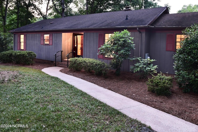 view of front facade with a shingled roof and a front lawn