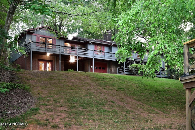 rear view of property featuring a garage, brick siding, a chimney, and a lawn