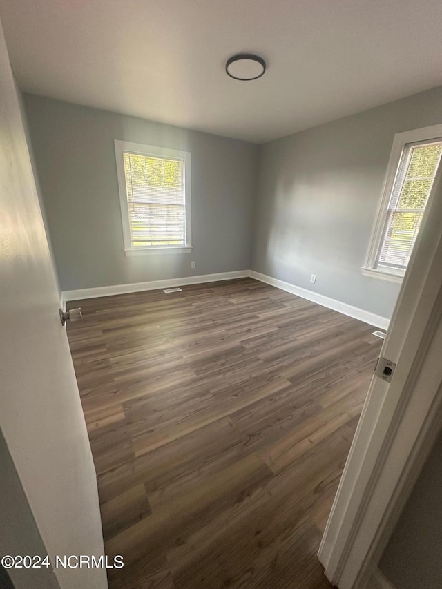 unfurnished room with dark wood-style floors, visible vents, and baseboards