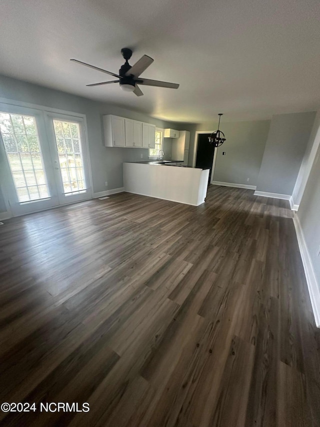 unfurnished living room with a ceiling fan, baseboards, and dark wood-type flooring