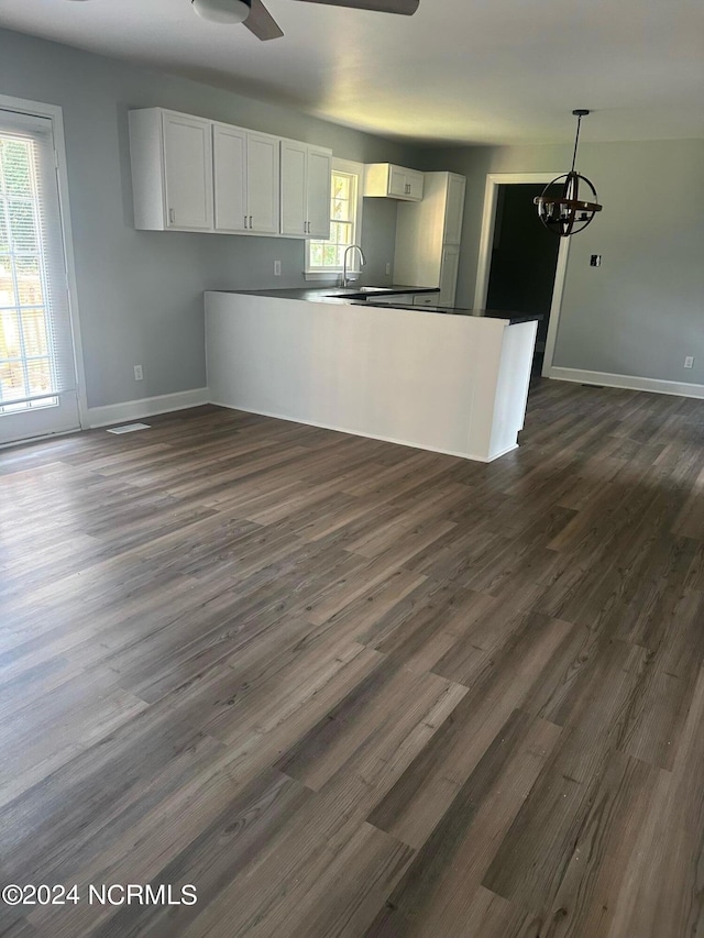 kitchen with a healthy amount of sunlight, white cabinets, dark wood-style flooring, and ceiling fan with notable chandelier