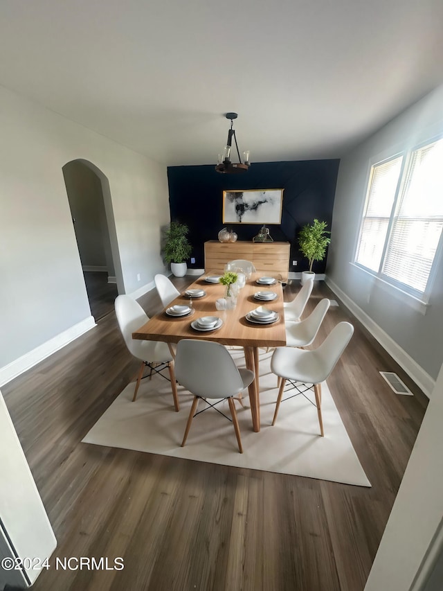 dining space with an inviting chandelier, baseboards, arched walkways, and wood finished floors