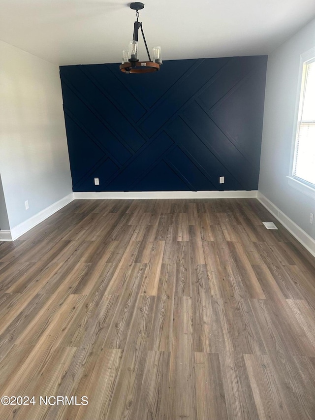 spare room with an inviting chandelier, baseboards, visible vents, and wood finished floors