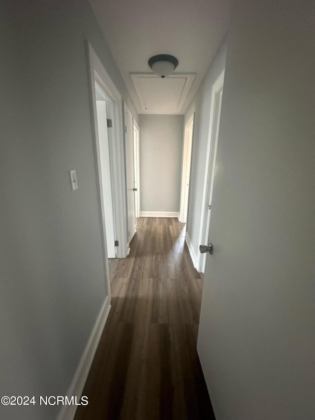 hallway featuring attic access, baseboards, and dark wood-style floors