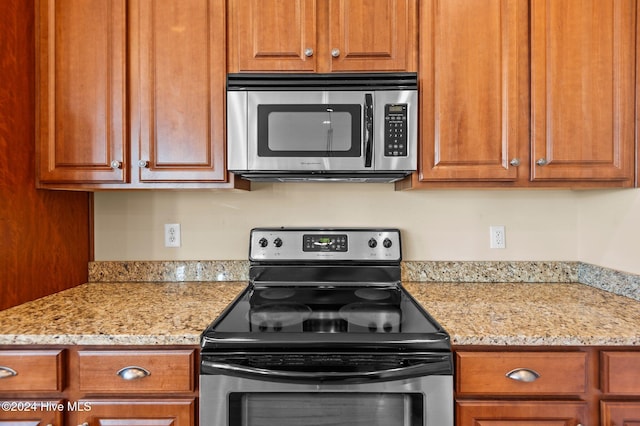 kitchen with stainless steel appliances, light stone counters, and brown cabinetry