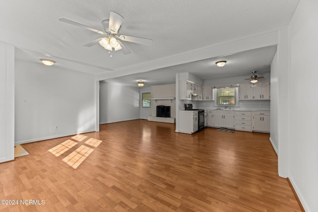 unfurnished living room featuring a textured ceiling, light hardwood / wood-style floors, ceiling fan, and sink