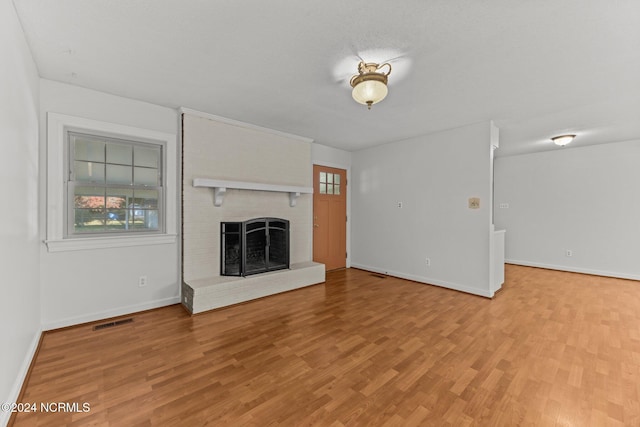 unfurnished living room with light wood-type flooring and a brick fireplace