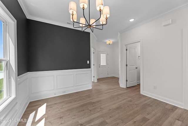 empty room featuring light wood finished floors, a chandelier, crown molding, and wainscoting